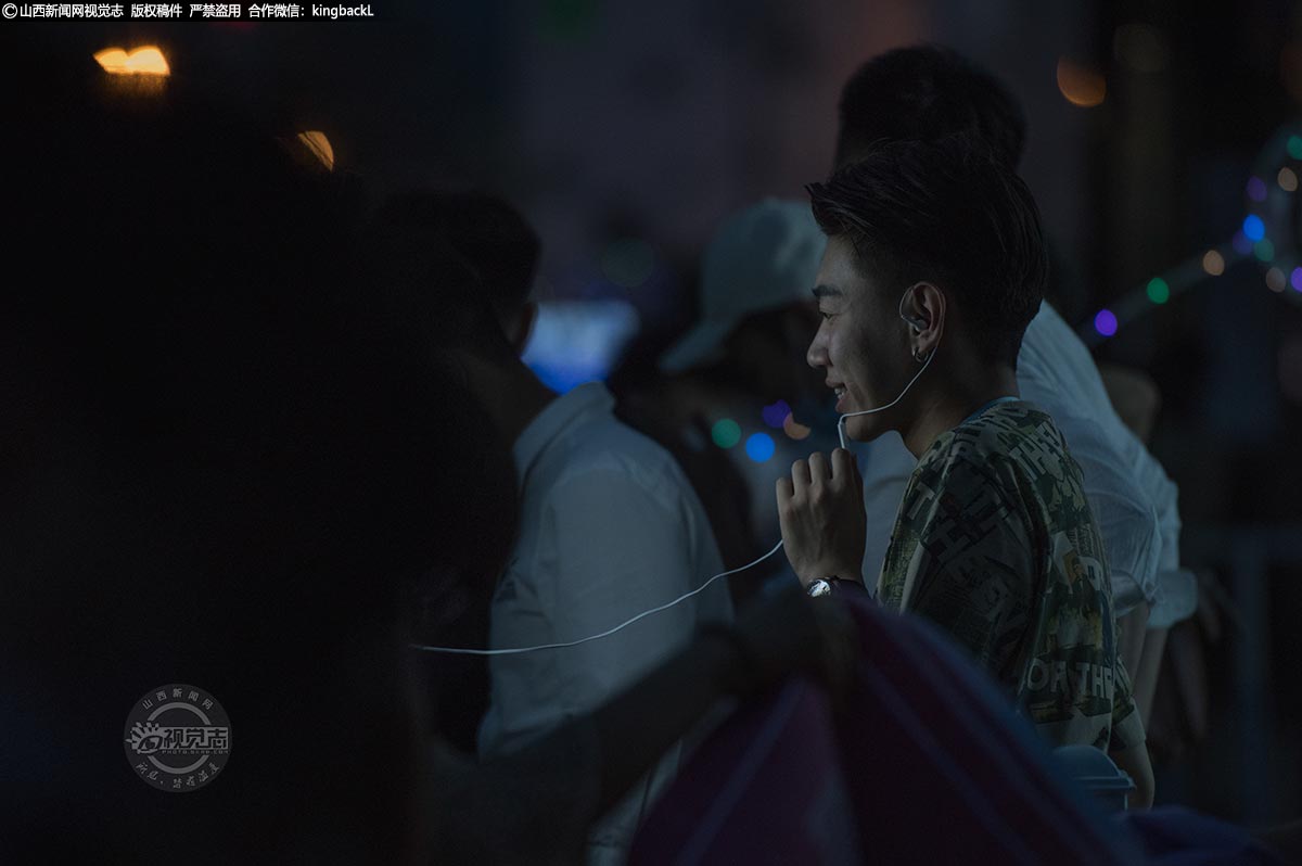      夜市是年轻人创业、直播带货、网红打卡的好去处。一位年轻人面前摆放着一套直播设备，正在通过一款短视频APP进行线上直播。夜市人来人往，很多人看到直播的网红都会好奇的停下脚步看一看。