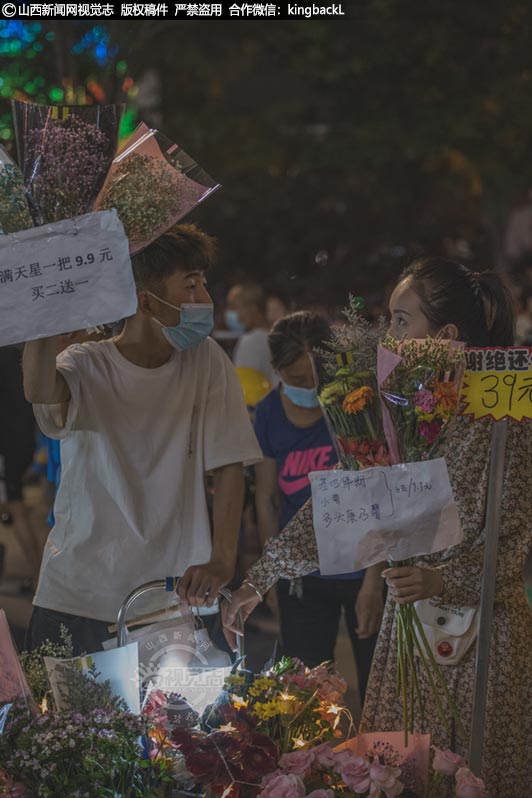      一对年轻人在夜市售卖干花，这种花又叫保鲜花、生态花，它保持了鲜花的特质，且颜色更为丰富保存时间长，深受年轻人的喜爱，所以这种干花也是夜市较为常见的商品。