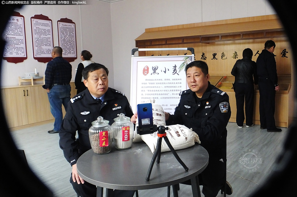      历经春夏秋冬和战“疫情”一年多艰难行程，山西省运城市新绛县古交镇闫家庄村，被村民誉为驻村“黑脸第一书记”的张卫东引进的扶贫黑小麦终于上市对外销售，按下了扶贫攻坚快进键。图为黑脸第一书记张卫东和县交警大队长张建学在村委黑小麦展柜前直播带货“黑小麦”产品。（■本期摄影：高新生）