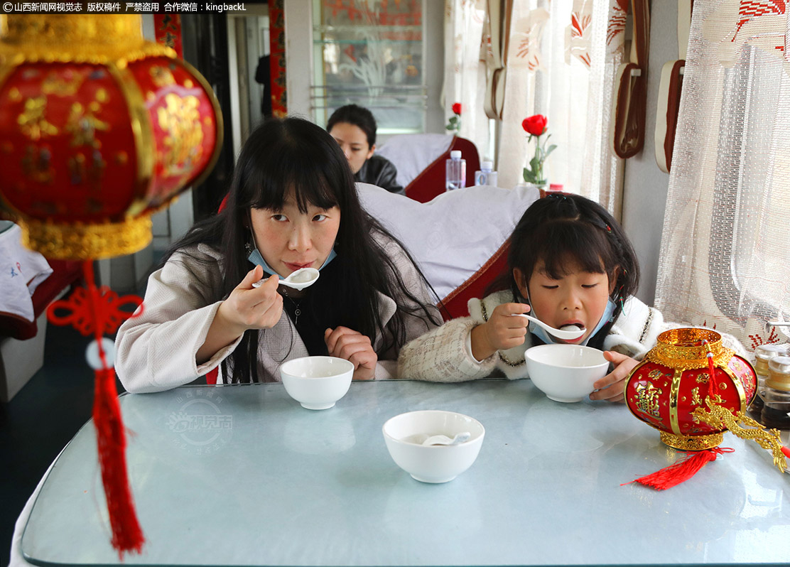      2月26日，是正月十五元宵节，餐车为旅客准备了刚出锅的元宵，乘客们没想到在火车上能吃到免费元宵，和其他旅客以及列车服务人员共度佳节，图为母女俩正高高兴兴品尝香甜可口的元宵。