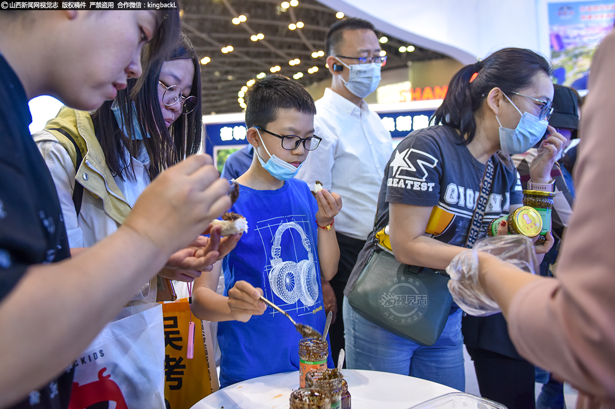      运城市花椒酱展位，一瓶瓶拧开瓶盖的花椒酱摆放在一张小桌子上，公司工作人员戴着一次性手套，捏起一块早已备好的馍块，抹上酱让人们品尝。运城市芮城县芮城适宜种花椒，当地的酱都是以优质花椒为主要原料，以石磨为主要生产工具，创新性地加入中药材、花生仁等创制的一种美食。其生产技艺属于运城市非物质文化遗产。