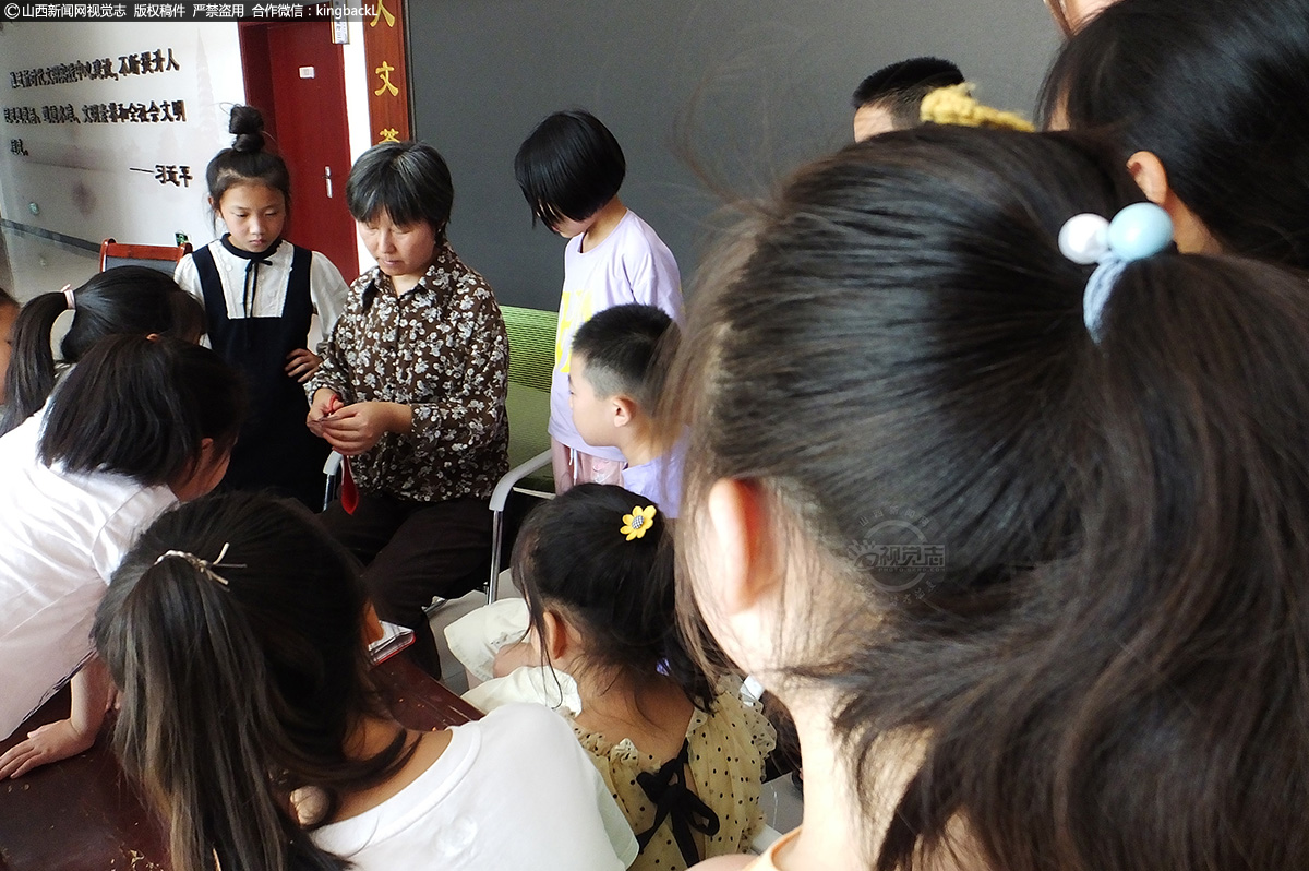      学生们围在剪纸大师段朋喆周围，观看学习她的非遗绛州剪纸技艺。绛州剪纸又称新绛剪纸，最早出现在春秋战国，它越过唐宋元清，走过改革开放，直到今天，没有随着时间的迁移消失在历史的长河中，反而更加具有韵味。