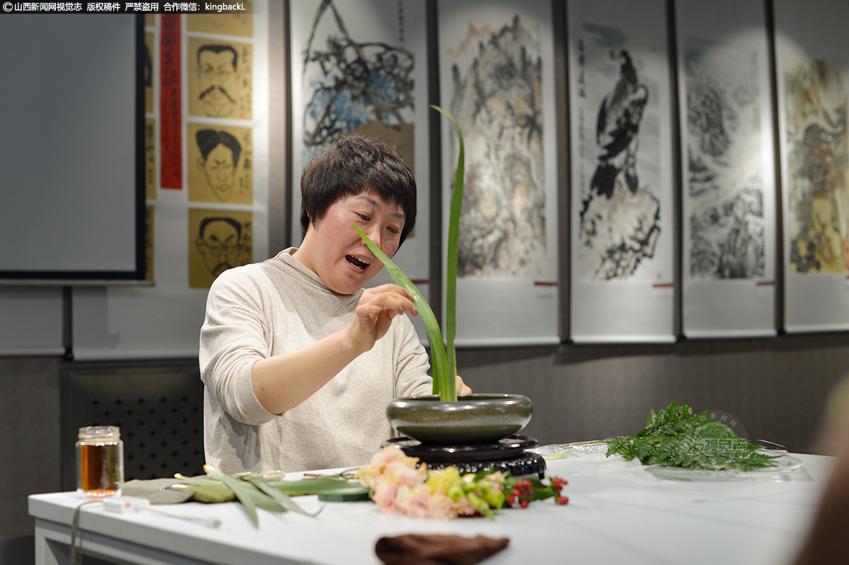      陈吉秀正在制作盘花直立式作品，通过植物花材的自然造型美态加以修饰，重组，尽显自然美，意境美。高低错落、动势呼应、俯仰顾盼、刚柔曲直，颇具自然韵味。插花自然多变、不拘泥于形式，顺乎自然之理、饱含自然之情、富有自然之趣。