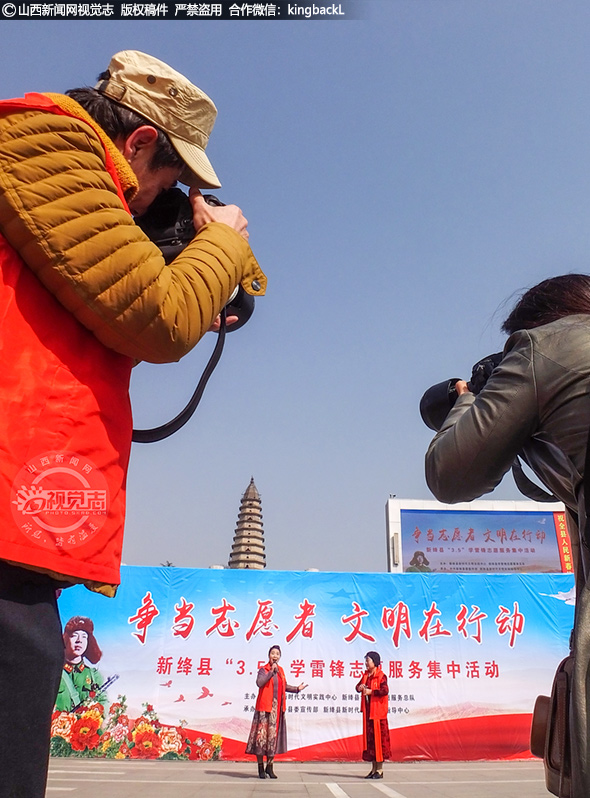      两名摄影师为台上表演的志愿者拍照留念。志愿者希望通过这次活动在社会上起到示范作用，让更多的爱心人士能够加入志愿者行列。