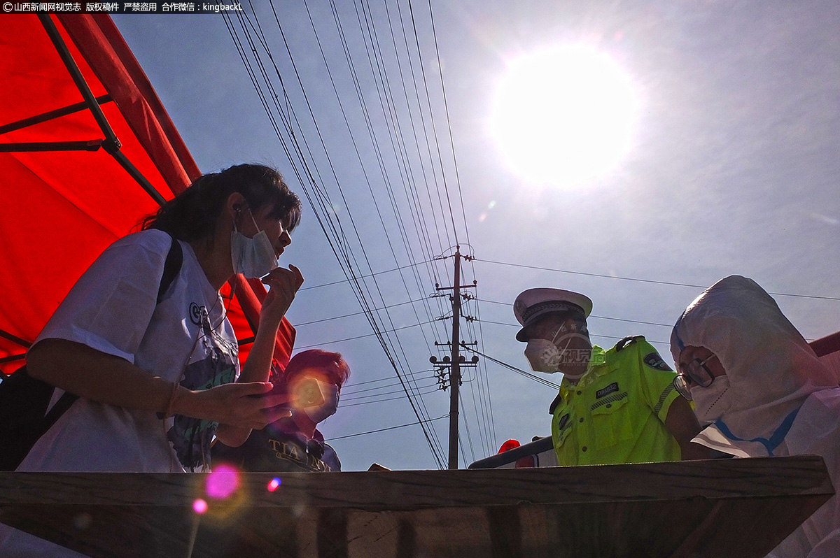      疫情防控检查站外，交警和防疫人员在高温下对入境人员扫码检测后登记行程等信息。