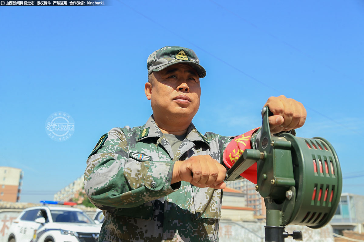      在防汛抗灾疏散安置行动现场，一位民兵正在操作手摇式警报器，群众在听到防空警报信号后，将迅速到达地面安全位置集合。
