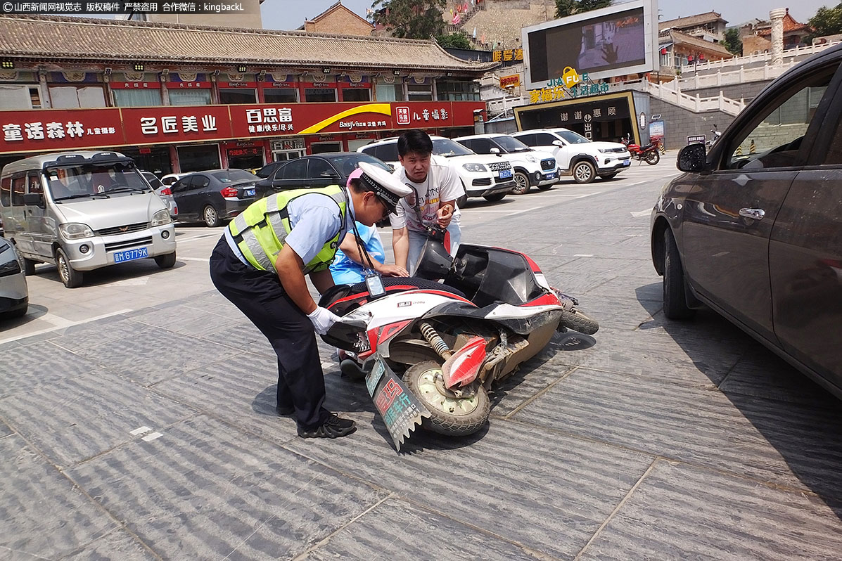      32岁的退伍军人辅警李刚红（左）头顶骄阳在山西运城市新绛县龙兴广场交通岗有序指挥交通。图为他正和一名青年快步将突然骑电动车摔倒的居民扶起。