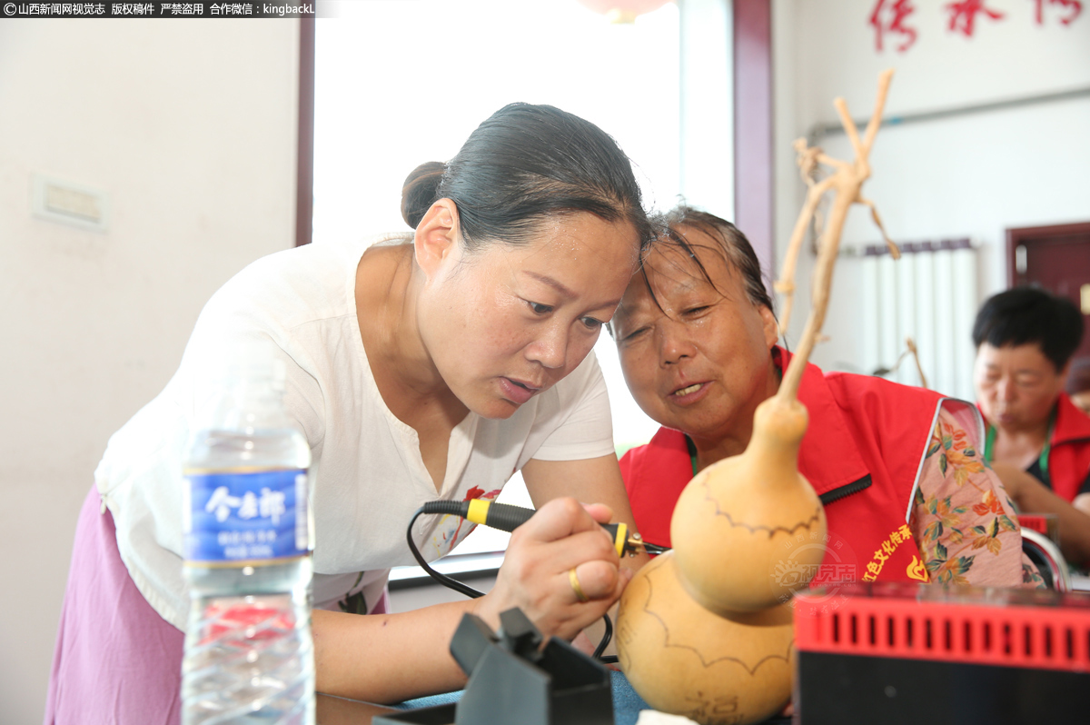      在自己的影响下，两个女儿大学毕业后返乡创业，也参与到了葫芦艺术的研究与开发中。图为薛改莲之女正在细心地为志愿者进行烙画示范。