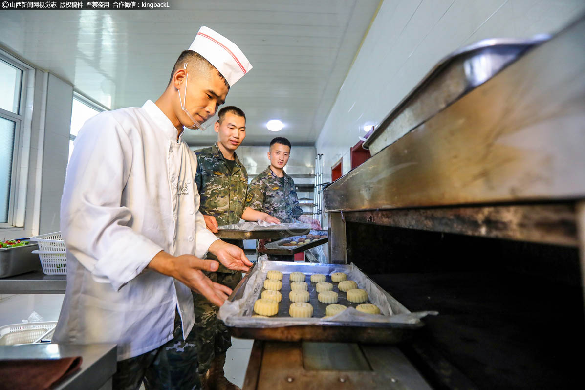      食堂的烤炉旁，官兵们正排队将成型的月饼依次放入，等待着月饼的成品。