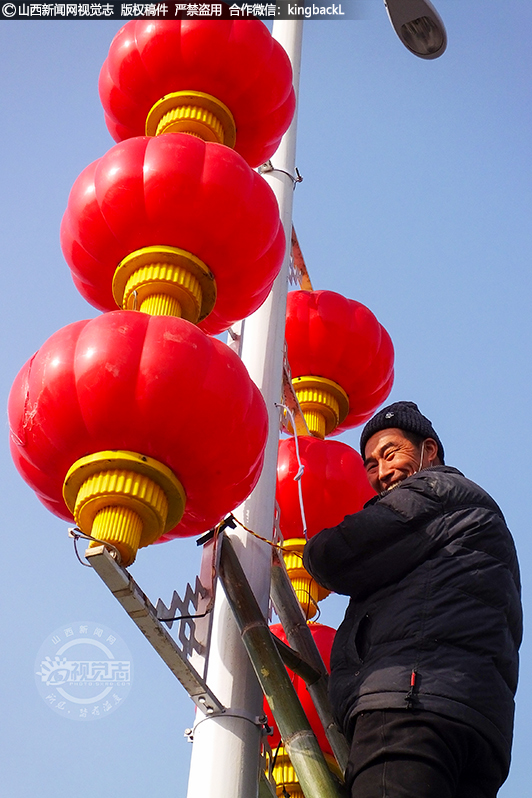      他们在脚手架上爬上爬下，将大红灯笼、中国结往灯杆上挂，并不时地找准角度，调整好位置。