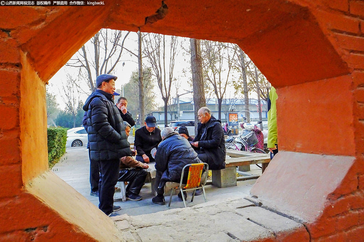      几名老年村民在休闲健身区打扑克聊天，享受着新铺设的柏油路带来的便利和舒适。