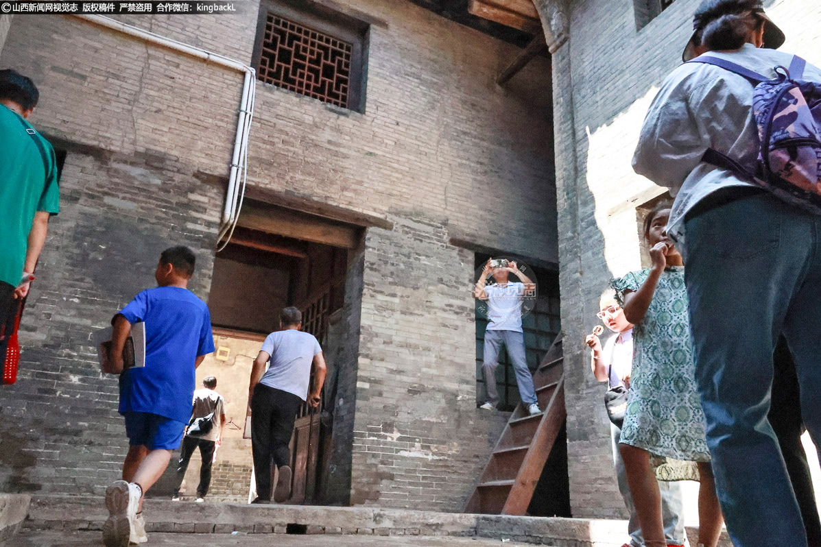      市民与游客在韩家巷6号院中院用手机记录古建砖雕照壁，阳光透过古建在地面形成几何光影。