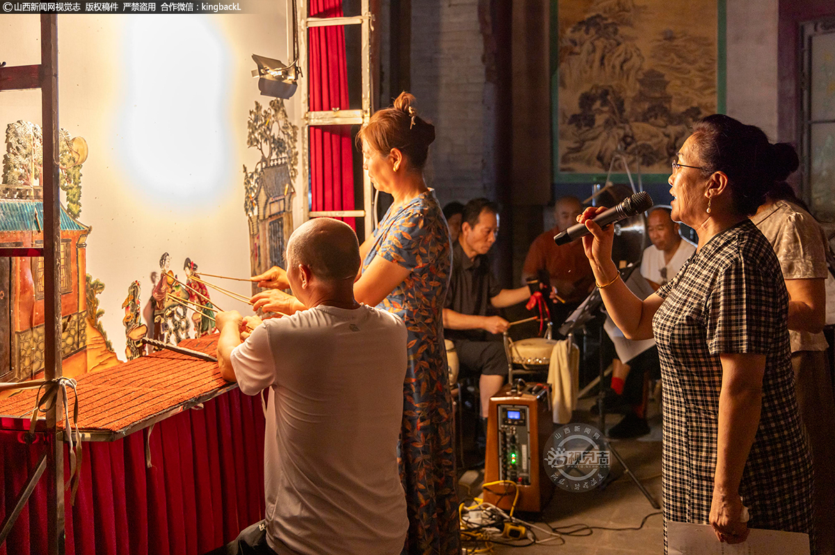      马世明、董柏兰在演绎，冯世香皮腔演唱《五更鸣》灯影戏。马世明的手指灵活地操控着三根竹杆，幕布上的人物时而蹙眉沉思，时而挥袖起舞，每一个动作都精准传神；董柏兰则专注于配合皮影的走位，让光影中的故事更具张力。
